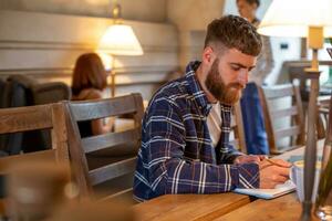 Casual business man or freelancer planning his work on notebook, working on laptop computer with smart phone, cup of coffee on table at coffee shop or home office. photo