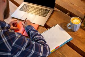 Cropped image of casual business man or freelancer planning his work on notebook, working on laptop computer with smart phone, cup of coffee on table at coffee shop or home office. photo