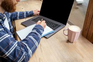 Cropped image of young man chatting via net-book during work break in coffee shop, male sitting in front open laptop computer with blank copy space screen. photo