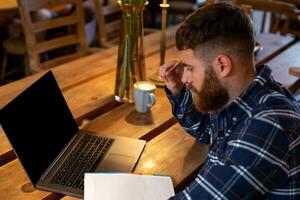 Young man chatting via net-book during work break in coffee shop, male sitting in front open laptop computer with blank copy space screen. photo