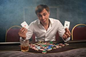 Handsome emotional man is playing poker sitting at the table in casino. photo