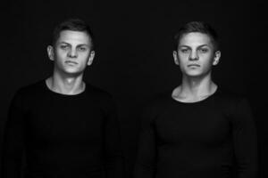 Two attractive positive young twin brothers standing dressed in photo