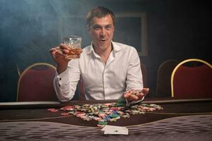 Handsome emotional man is playing poker sitting at the table in casino. photo