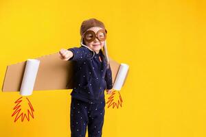 Freedom, girl playing to be airplane pilot, funny little girl with aviator cap and glasses, carries wings made of brown cardboard as an airplane photo