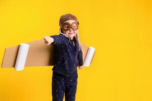 Freedom, girl playing to be airplane pilot, funny little girl with aviator cap and glasses, carries wings made of brown cardboard as an airplane photo