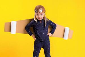 libertad, niña jugando a ser avión piloto, gracioso pequeño niña con aviador gorra y anteojos, lleva alas hecho de marrón cartulina como un avión foto