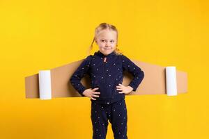 un pequeño niño niña es vistiendo hecho en casa cartulina volador alas, fingiendo a ser un piloto para un artesanía, imaginación o exploración concepto. foto