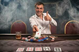 Handsome emotional man is playing poker sitting at the table in casino. photo