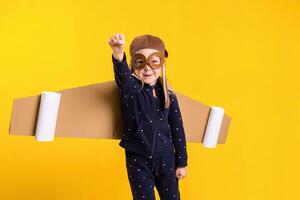 Freedom, girl playing to be airplane pilot, funny little girl with aviator cap and glasses, carries wings made of brown cardboard as an airplane photo