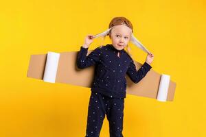 un pequeño niño niña es vistiendo hecho en casa cartulina volador alas, fingiendo a ser un piloto para un artesanía, imaginación o exploración concepto. foto