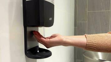 vrouw desinfecteren haar handen. vrouw handen gebruik een tintje antiseptisch dispenser. op de muur gemonteerd dispenser met ontsmettingsmiddel in een boodschappen doen centrum. een vrouw behandelt haar handen met antiseptisch. video