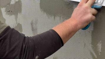 Close-up of a worker's hand with a trowel applying mortar to reinforcing mesh and rigid polyurethane foam for home insulation. A worker plasters with a metal spatula. Insulation of walls. video