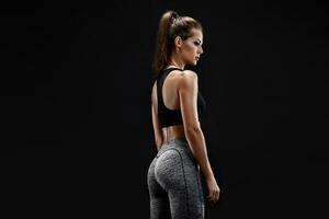 Shot of a strong woman with muscular abdomen in sportswear. Fitness female model posing on black background. photo