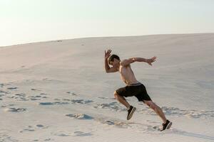Fit man running fast on the sand. Powerful runner training outdoor on summer. photo