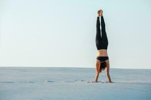 Young woman practicing inversion balancing yoga pose handstand on sand. photo