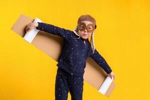 Freedom, girl playing to be airplane pilot, funny little girl with aviator cap and glasses, carries wings made of brown cardboard as an airplane photo