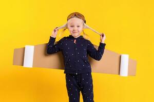 libertad, niña jugando a ser avión piloto, gracioso pequeño niña con aviador gorra y anteojos, lleva alas hecho de marrón cartulina como un avión foto