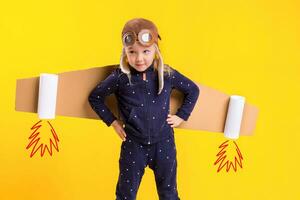 Freedom, girl playing to be airplane pilot, funny little girl with aviator cap and glasses, carries wings made of brown cardboard as an airplane photo