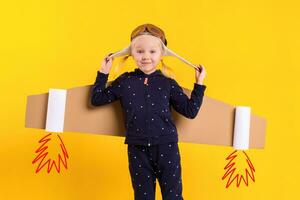 Freedom, girl playing to be airplane pilot, funny little girl with aviator cap and glasses, carries wings made of brown cardboard as an airplane photo