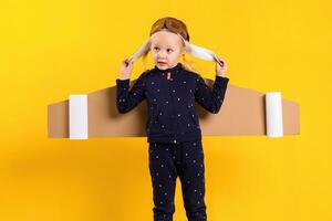 A little child girl is wearing homemade cardboard flying wings, pretending to be a pilot for a craft, imagination or exploration concept. photo