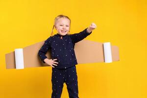 un pequeño niño niña es vistiendo hecho en casa cartulina volador alas, fingiendo a ser un piloto para un artesanía, imaginación o exploración concepto. foto