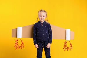 A little child girl is wearing homemade cardboard flying wings, pretending to be a pilot for a craft, imagination or exploration concept. photo