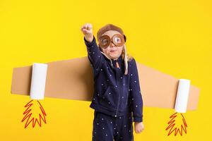 Freedom, girl playing to be airplane pilot, funny little girl with aviator cap and glasses, carries wings made of brown cardboard as an airplane photo