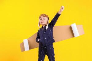 Freedom, girl playing to be airplane pilot, funny little girl with aviator cap and glasses, carries wings made of brown cardboard as an airplane photo