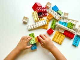 Child playing with colorful building blocks on white background. Top view photo