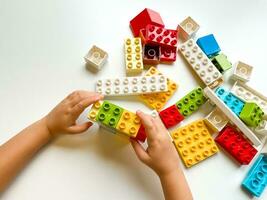 Child playing with colorful building blocks on white background. Top view photo