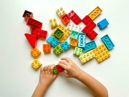 Child playing with colorful building blocks on white background. Top view photo