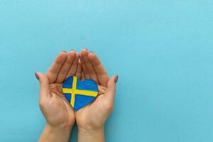 Paper heart in the colors of the flag of Sweden in female hands. photo