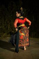 a Javanese dancer wearing a black shawl and jasmine on her head while dancing on stage at night photo