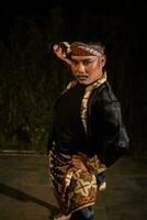 a male dancer wearing a black costume full of batik patterns with make-up on his face photo