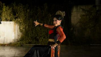 a Balinese dancer dances under the stage lights which highlight her red dress and create an elegant visual photo