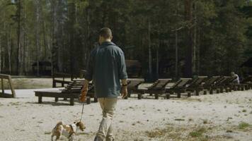 Man walks with dog on beach in woods. Stock footage. Man walks with his dog on sand at resort in summer. Man with dog walking on shore of pond in forest on sunny summer day photo