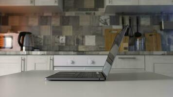 Concept of working at home during isolation. Action. Side view of male hands openning new silver laptop that is standing on the white table in the kitchen. photo