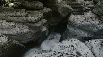 Water stream of mountainous river flowing between rocks in the narrow gorge. Clip. Water stream with cold fresh water and many white boulders. photo