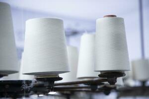 White Cotton Spools of Thread on the industrial knitting factory machine stand photo