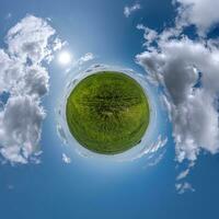 green tiny planet in blue sky with beautiful clouds. Transformation of spherical panorama 360 degrees. Spherical abstract aerial view. Curvature of space. photo