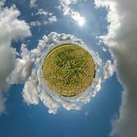 green tiny planet in blue sky with beautiful clouds. Transformation of spherical panorama 360 degrees. Spherical abstract aerial view. Curvature of space. photo