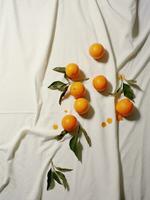 AI generated eight tangerines on white cloth, with green leaves, everyday ephemera, organic material photo