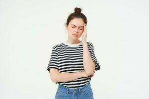 Portrait of tired woman rubs her forehead, touches head, has a headache, stands distressed against white background photo