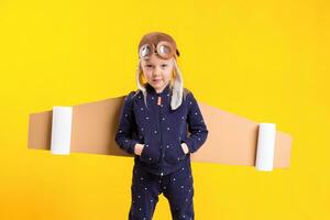 libertad, niña jugando a ser avión piloto, gracioso pequeño niña con aviador gorra y anteojos, lleva alas hecho de marrón cartulina como un avión foto