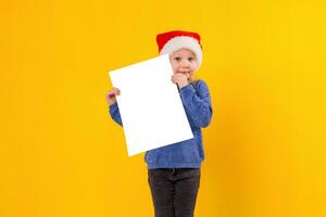 linda pequeño niña en Papa Noel claus sombrero con un blanco blanco papel hoja. Navidad, Navidad, nuevo año, invierno, gente, anuncio publicitario, rebaja concepto. foto