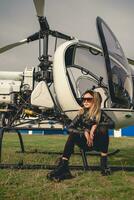 Confident blonde tween girl sitting on landing skids of helicopter photo