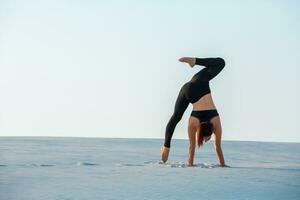 Young woman practicing inversion balancing yoga pose handstand on sand. photo