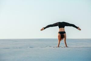 joven mujer practicando inversión equilibrio yoga actitud parada de manos en arena. foto