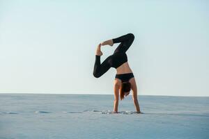 Young woman practicing inversion balancing yoga pose handstand on sand. photo