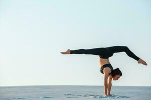 Young woman practicing inversion balancing yoga pose handstand on sand. photo